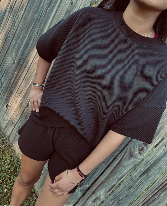 Full length view of a Black ribbed set of a girl in front of a fence standing in the grass.