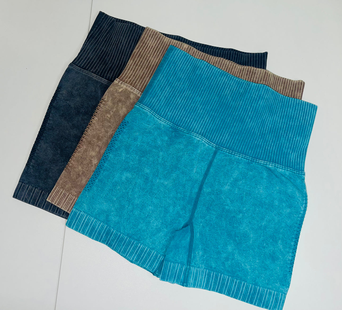 High-waisted seamless biker shorts in teal, black, and brown laid flat on a white background