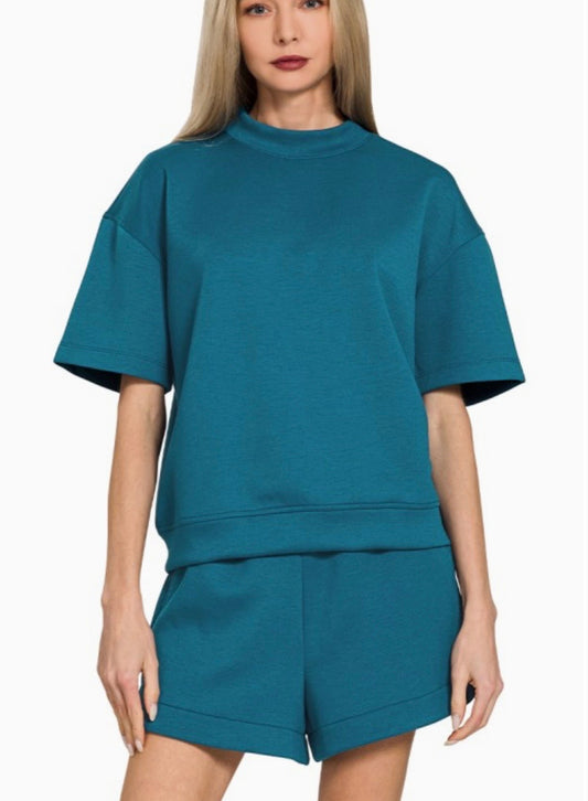 Model wearing a teal lounge set featuring a relaxed short sleeve top and matching elastic waistband shorts, and a white background.