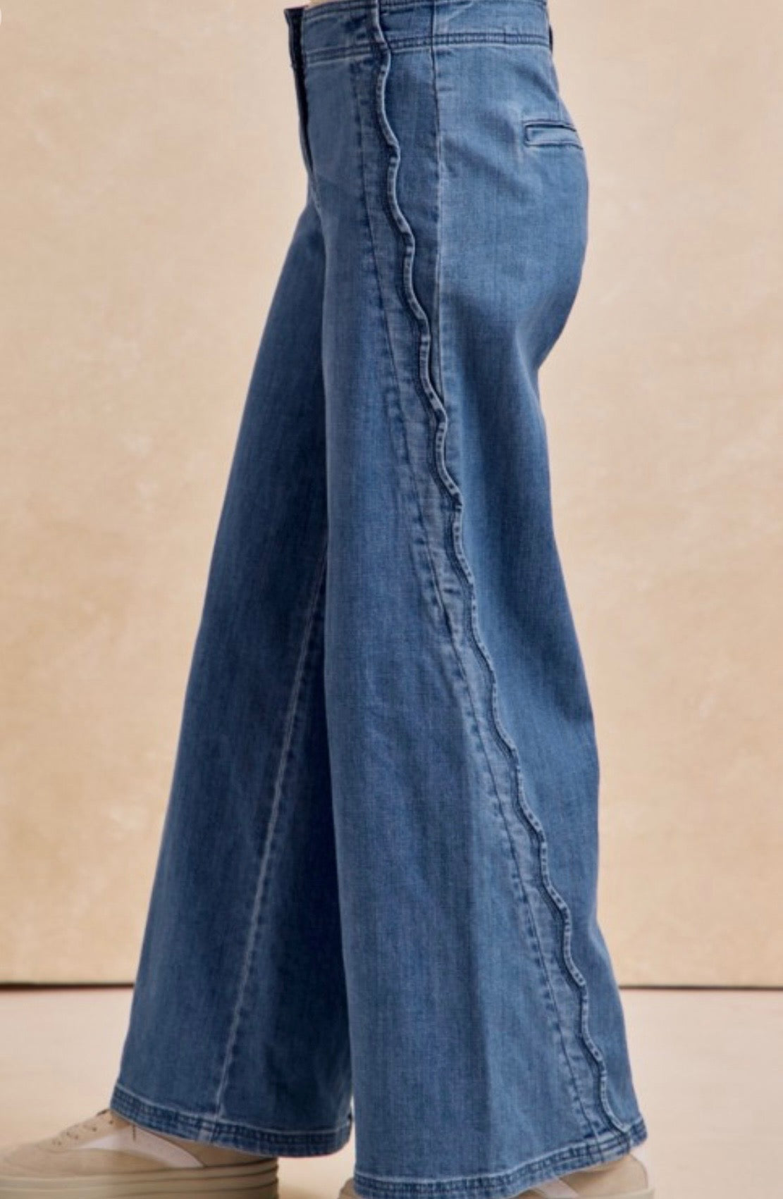 Blue jeans with a wavy scalloped detail on a beige background.