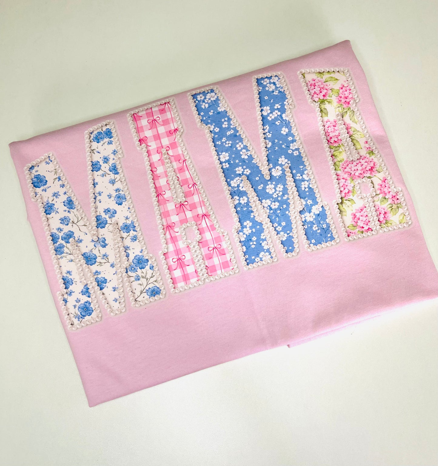 Fabric with floral and checkered letters spelling 'M' on a pink background