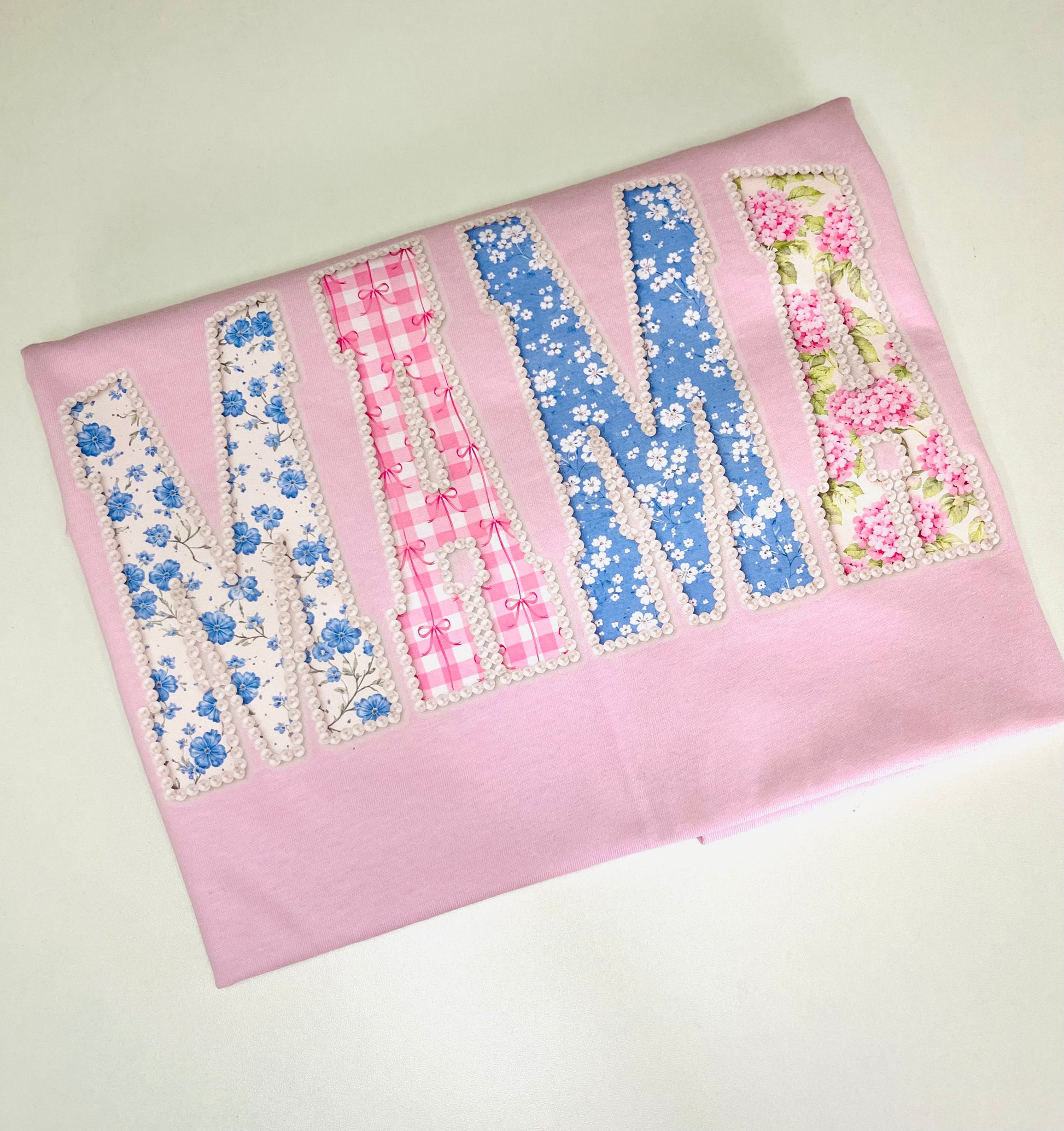 Fabric with floral and checkered letters spelling 'M' on a pink background