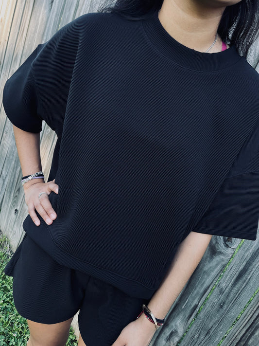 Full length view of a Black ribbed set of a girl in front of a fence standing in the grass.