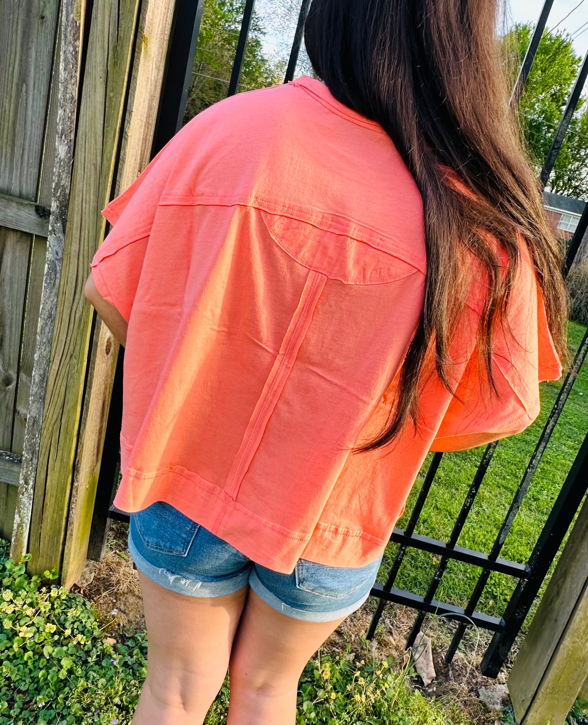 Person wearing a coral shirt and denim shorts standing outdoors.