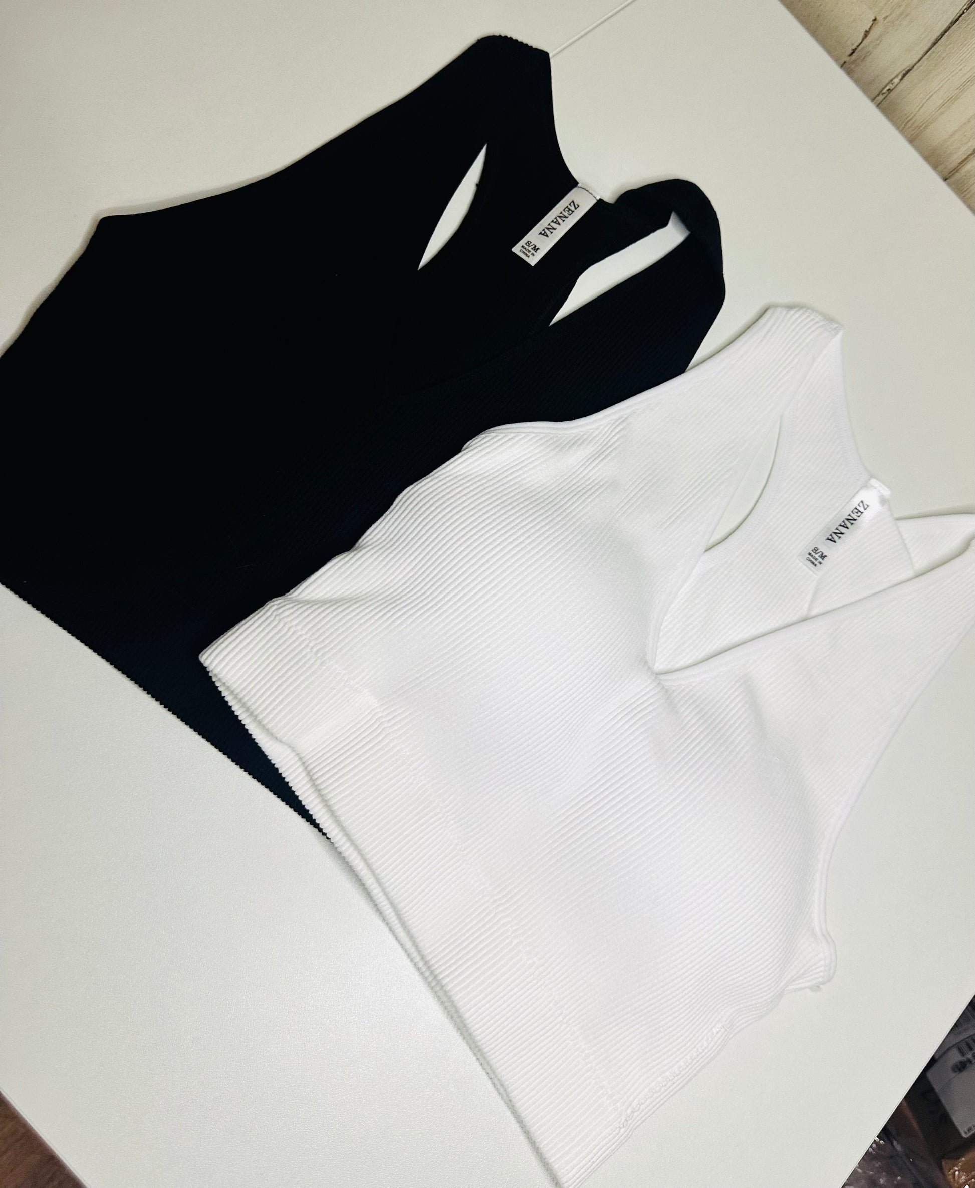 Black and white ribbed tops laid flat on a white surface, tank top and a fitted silhouette.