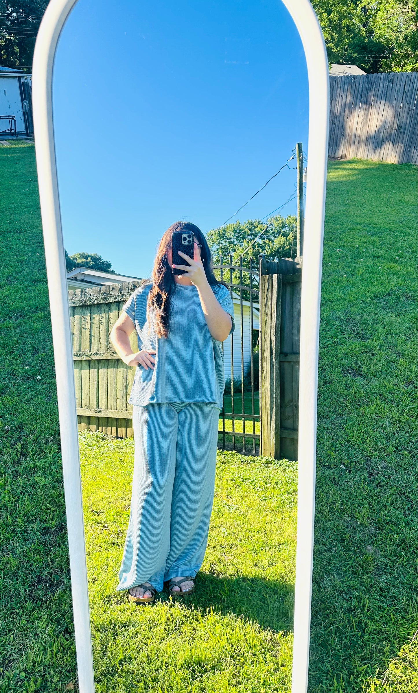 Model wearing a light blue ribbed lounge set featuring a loose short-sleeve top and wide-leg pants, photographed outdoors in a full-length mirror on grass.